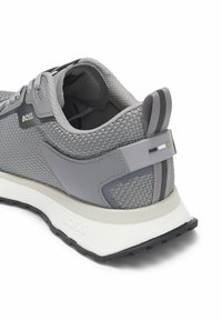 Szary sportowy but z siateczki z wyściełanym kołnierzem, czarno-białą podeszwą, pętelką z paskami oraz logo "BOSS" po boku i na pięcie.