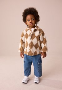 Braun-weiß karierte, flauschige Jacke mit Kragen, kombiniert mit blauen Cargo-Jeans und weißen Sneakers.