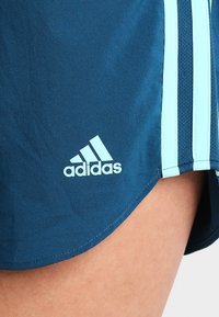 Pantalones cortos deportivos de color marino con rayas azul claro y un logo de Adidas bordado en blanco en la parte inferior delantera. El material parece suave y ligero.
