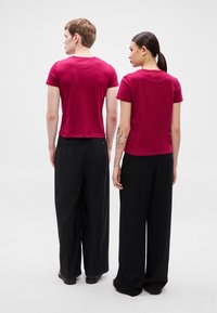 Trička s krátkým rukávem v barvě burgundské červené, kombinovaná s volnými černými kalhotami. Trička mají jednoduchý design s kulatým výstřihem a krátkým střihem.