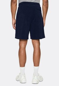 Shorts in spugna blu navy con una texture morbida, vita elastica e tasche laterali, abbinati a sneakers bianche e calze.