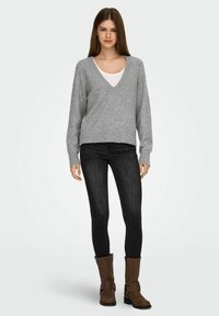 Sivi pulover z V-izrezom in dolgimi rokavi, oblečen čez belo majico, v kombinaciji s črnimi ožjimi jeans hlačami in rjavimi ankel škornji. Preprost dizajn in tekstura.