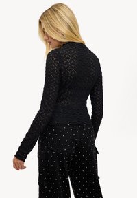 Haut noir à manches longues avec un design texturé et à motifs. Associé à un pantalon noir orné de pois blancs et doté de poches.