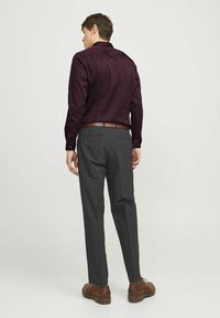 Bordeaux kleurige button-up shirt met lange mouwen, gecombineerd met donkere grijze broek. Bruine leren schoenen en riem. Model wordt van achteren getoond.