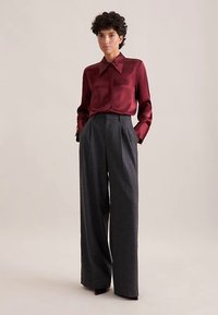 Blusa di seta color bordeaux con colletto abbinata a pantaloni grigi a vita alta, a gamba larga, con tessuto strutturato e pieghe frontali.