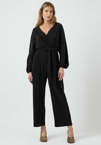 Jumpsuit negro plisado con envoltura, de manga larga, cintura ajustada y corte recto en las piernas. La tela presenta un diseño texturizado.