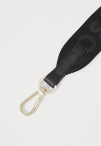 Cinturino in tessuto nero con logo impresso, dotato di una sezione in pelle liscia e una clip in metallo color oro per il fissaggio. Texture morbida.