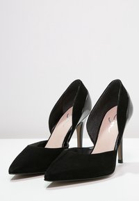 Černé vysoké podpatky s špičatou špičkou a výřezem po stranách. Vyrobené z vepřovice a lakované kůže, s elegantním designem a štíhlým jehlovým podpatkem.