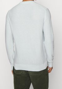 Helles blaues Strickpullover mit Rundhalsausschnitt, langen Ärmeln und gerippten Bündchen. Das Design besteht aus einem strukturierten, atmungsaktiven Stoff.