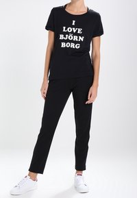 Camiseta negra con el texto blanco "I LOVE BJÖRN BORG," combinada con pantalones negros. El modelo lleva zapatillas blancas, mostrando un atuendo casual.