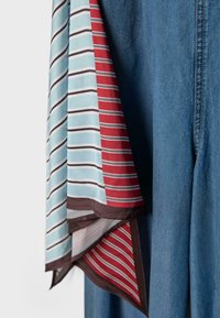 Tissu rayé avec des sections bleu clair, rouge et marron, suspendu à côté d'un pantalon en denim bleu avec des coutures visibles.