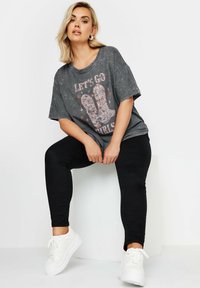 Harmaa ylisuurta T-paitaa, jossa on "Let's Go Girls" -grafiikka ja vaaleanpunaisia yksityiskohtia, yhdistetty mustiin farkkuihin ja valkoisiin tennareihin. Sujuva tekstuuri, rento istuvuus.