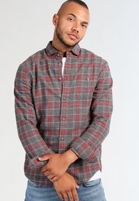 Camisa de franela a cuadros en tonos rojo y gris con cierre de botones, mangas largas y un bolsillo en el pecho. La tela parece suave y texturada.