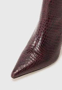 Stivale alto con tacco a puntale in borgogna, realizzato in un materiale sintetico lucido con texture in finta coccodrillo e dettagli di cucitura discreti. Design elegante e strutturato.