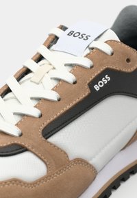Witte en tan sneakers met grijze accenten. Voorzien van canvas en suède materialen, vetersluiting en opvallende "BOSS" branding. Zwarte loopzool.