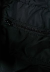 Tejido de nylon negro con un bolsillo con cremallera horizontal y herrajes negros resistentes. La textura es suave con un ligero brillo.