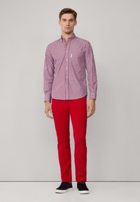 Pantalones de algodón rojos combinados con una camisa de botones de rayas en tonos rojos y blancos, que presenta un collar con solapa y mangas largas.