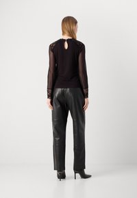 Haut noir avec manches longues transparentes, accents en dentelle aux épaules et aux poignets, détail dos en keyhole ; associé à un pantalon en cuir noir taille haute.