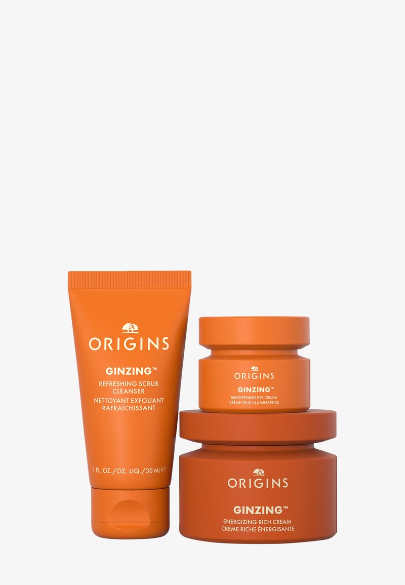 Trois produits de soin de la peau dans un emballage orange : un tube de nettoyant exfoliant et deux pots (un plus grand et un plus petit) étiquetés "Ginzng."