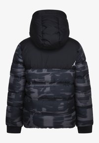 Chaqueta acolchada negra con capucha, con un acabado mate, rayas horizontales en diferentes tonalidades y un pequeño logo en la parte superior izquierda.