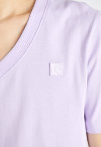 Lavendel V-hals T-shirt i mjuk bomull, med korta ärmar och en texturerad, broderad logotyp på vänster sida.