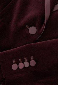 Burgundi bársonykabát, egygombos záródással és négy díszgombbal, sima textúrával és letisztult dizájnnal.