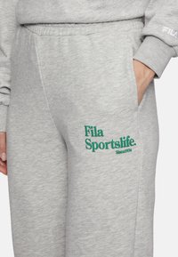 Grijze sweatpants met een zachte textuur, met een groen geborduurd logo "Fila Sportslife. Sinds 1974" op de linker bovenbeen. Elastische tailleband.