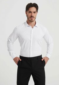 Chemise blanche à manches longues avec un devant à boutons, un col pointu et des poignets noirs contrastants, associée à un pantalon noir ajusté.