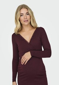 Robe portefeuille à manches longues en tissu côtelé bordeaux avec une bordure en dentelle au niveau du col, présentant une silhouette ajustée et une texture douce.