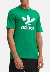 T-shirt in cotone verde con grande logo Adidas trefoil bianco, maniche corte e scollatura tonda. Tessuto liscio e vestibilità regolare.