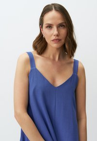 Top senza maniche blu con design a V, tessuto liscio e leggera drappeggiatura nella parte inferiore. Presenta spalline larghe.