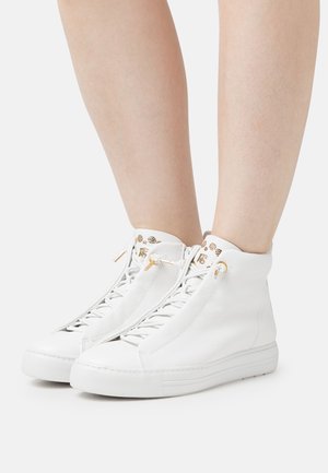 Baskets montantes blanches en cuir texturé, avec des accents en métal doré et un design épuré et minimaliste.
