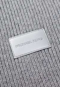 Tessuto in maglia grigio con texture a coste verticali, caratterizzato da una prominente etichetta in pelle bianca impressa con la scritta "MICHAEL KORS."