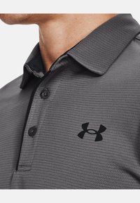 Polo shirt grigio texturizzato con colletto nero, dotato di due bottoni e un logo nero sul petto.