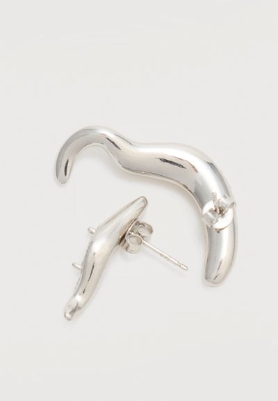 Boucles d’oreilles puces courbées abstraites de ton argenté avec des formes lisses et irrégulières, présentées sur un fond blanc uni.