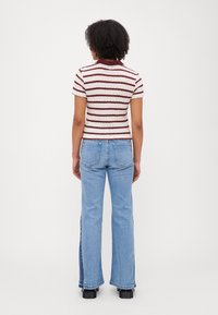 Kortermet, ribbestrikket topp med maroon og hvite striper, kombinert med høy midje lys blå, utsvingte jeans. Flate svarte sko inkludert.