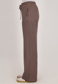 Bruine, lichtgewicht, broek met trekkoord en een textuur oppervlak, voorzien van zijzakken en een relaxte pasvorm, gedragen met casual schoenen.