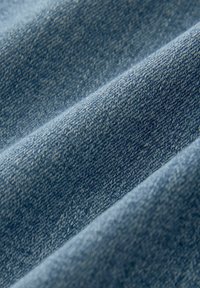 Nära bild av blå denimtyg som visar detaljerad vävstruktur och mjuka veck.