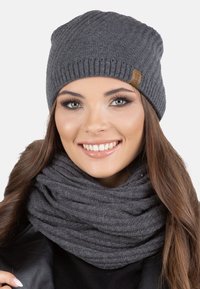 Berretto di maglia grigio con texture a coste e una piccola etichetta in pelle. Sciarpa chunky grigia abbinata con un motivo a maglia testurizzato.