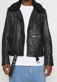 Sort læder motorcykeljakke med en faux shearling krave, lynlåslommer, spænde rem i kanten og sølv hardware detaljer.