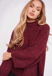Burgundy knitted sweater with a high neckline, long sleeves, and ribbed edges. Features a textured, cozy fabric and a relaxed fit.