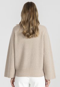 Beżowy sweter prążkowany z szerokimi rękawami i luźnym krojem. Tekstura jest miękka i dziana, z prostym dołem i minimalnymi detalami.