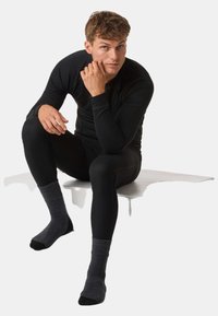 Czarna termiczna warstwa bazowa z prążkowaną strukturą, długimi rękawami i dopasowanym krojem. Szare skarpetki z ciemnymi akcentami, leżące na białej powierzchni.