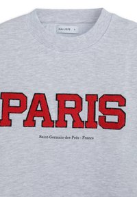 Sweatshirt gris avec "PARIS" en broderie rouge en gras, et "Saint-Germain-des-Prés - France" en texte plus petit en dessous.