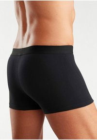 Schwarze Baumwoll-Boxershorts mit einer glatten Textur und elastischem Bund, die ein enges Design und minimale Nähte aufweisen.