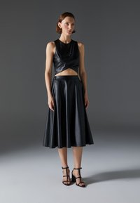 Svart läder cropped topp med en vriden design, kombinerad med en flödande svart läderkjol och svarta strappy klackar. Slät, elegant textur.