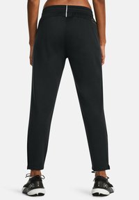 Zwarte sportieve broek met een taps toelopend ontwerp, elastische tailleband, ritssluiting achterzak en details bij de enkels. Draagt samen met zwart-witte sportschoenen.