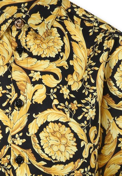 Maglietta a maniche corte con uno sfondo nero e un motivo floreale e fogliare giallo, chiusura con bottoni e texture di tessuto liscia.