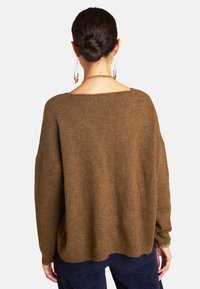 Brauner oversized Pullover mit lockerer Passform, weitem Ausschnitt und gestrickter Textur. Die Rückseite weist einen subtilen Schimmer auf. Lange Ärmel.