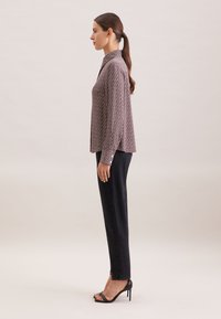 Blouse à manches longues et col, avec un motif géométrique rose et blanc, associée à un jean noir taille haute et des sandales à talons aiguilles noires.